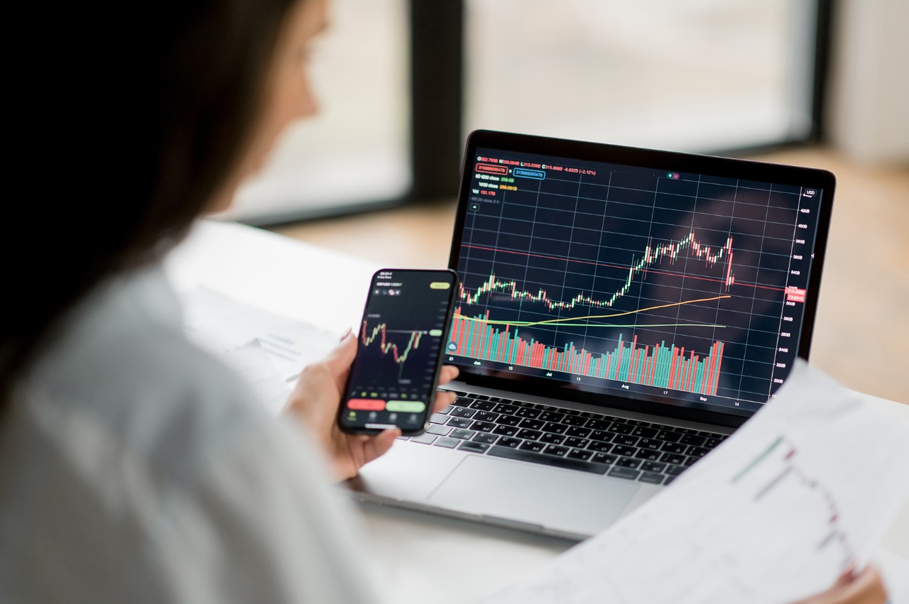 Une femme analysant des graphiques de la bourse sur un ordinateur et un téléphone 