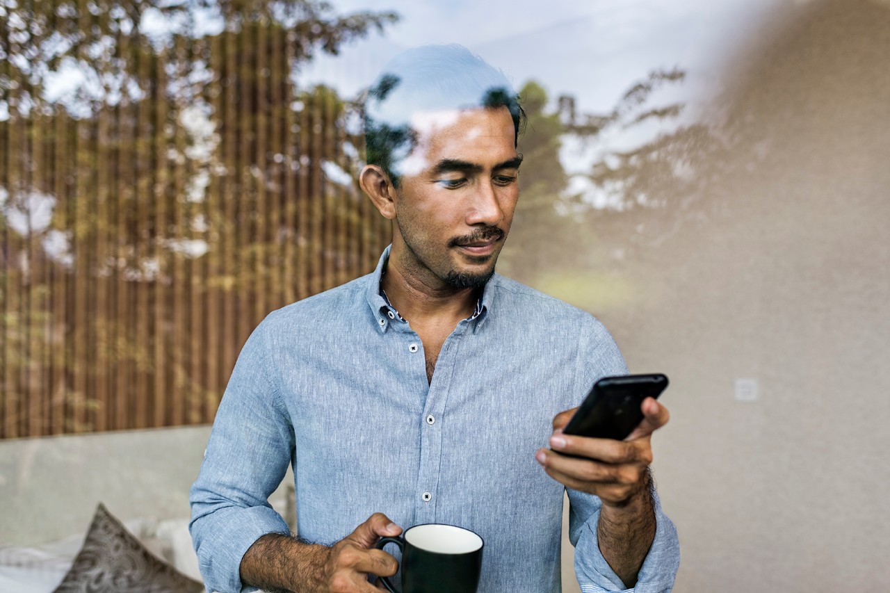 Un homme regardant son téléphone pendant qu'il boit son café
